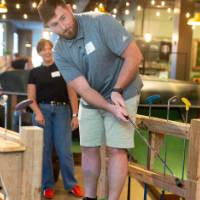 Man swinging golf club as three other event attendees look on